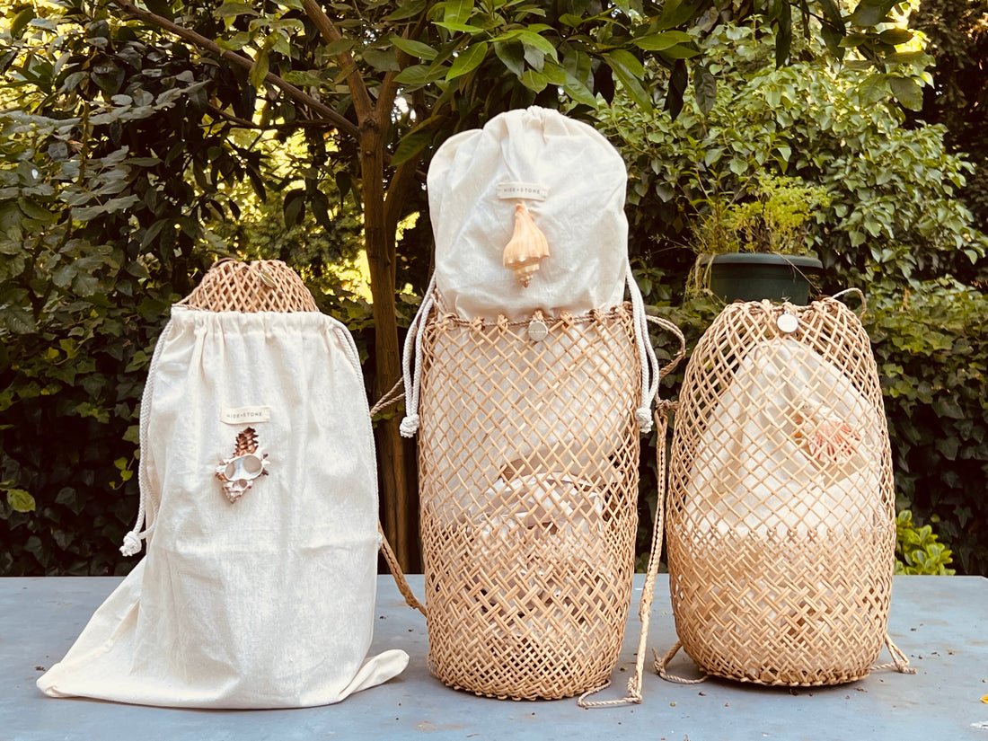 Three handwoven rattan basket bags in varying sizes, paired with organic cotton canvas dust bags featuring signature shell accents.