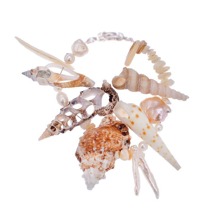 Handcrafted statement bracelet featuring an organic arrangement of natural sea shells and luminous baroque pearls on a white background.