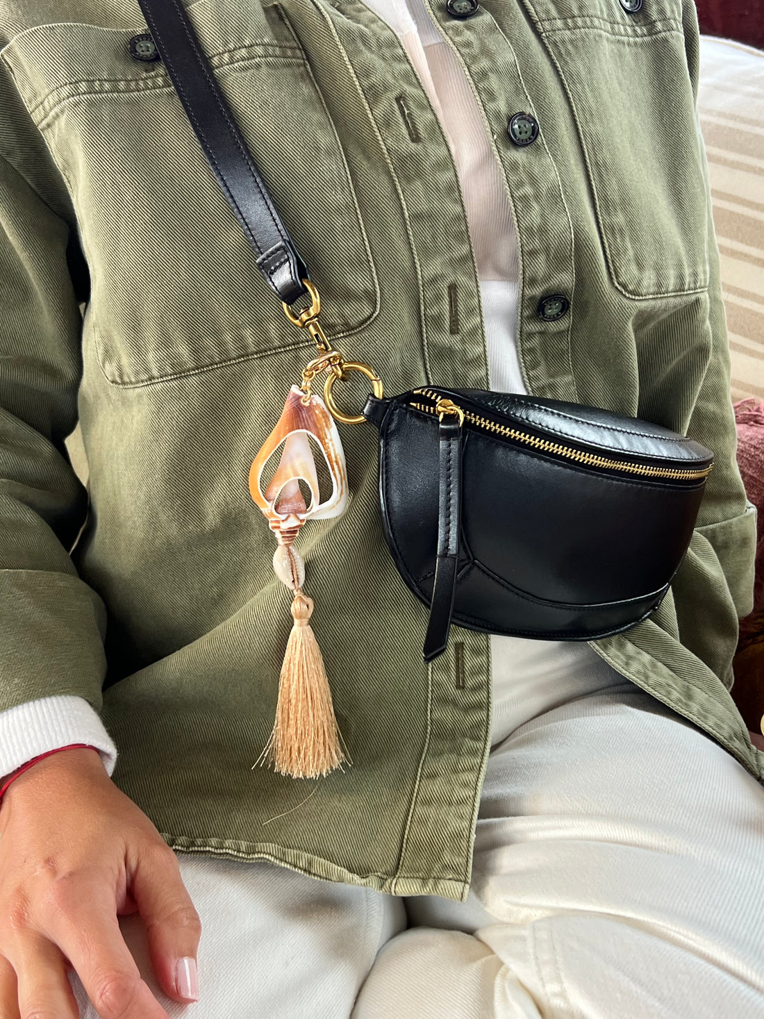 Handmade shell fob featuring a white cut natural murex shell, a small cowrie, and a beige cotton tassel on a gold-toned ring styled on a black bag
