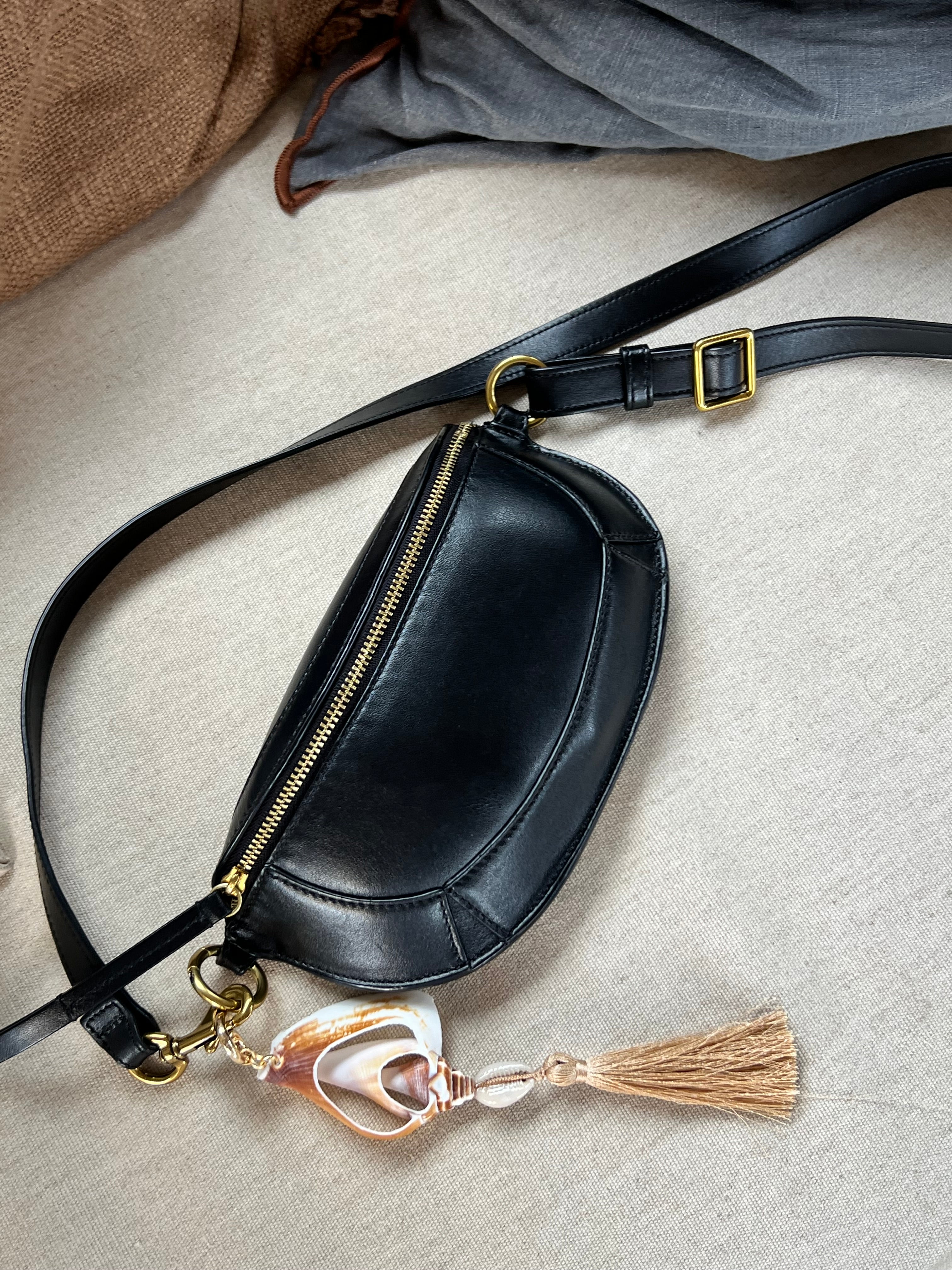 Handmade shell fob featuring a white cut natural murex shell, a small cowrie, and a beige cotton tassel on a gold-toned ring styled on a black bag