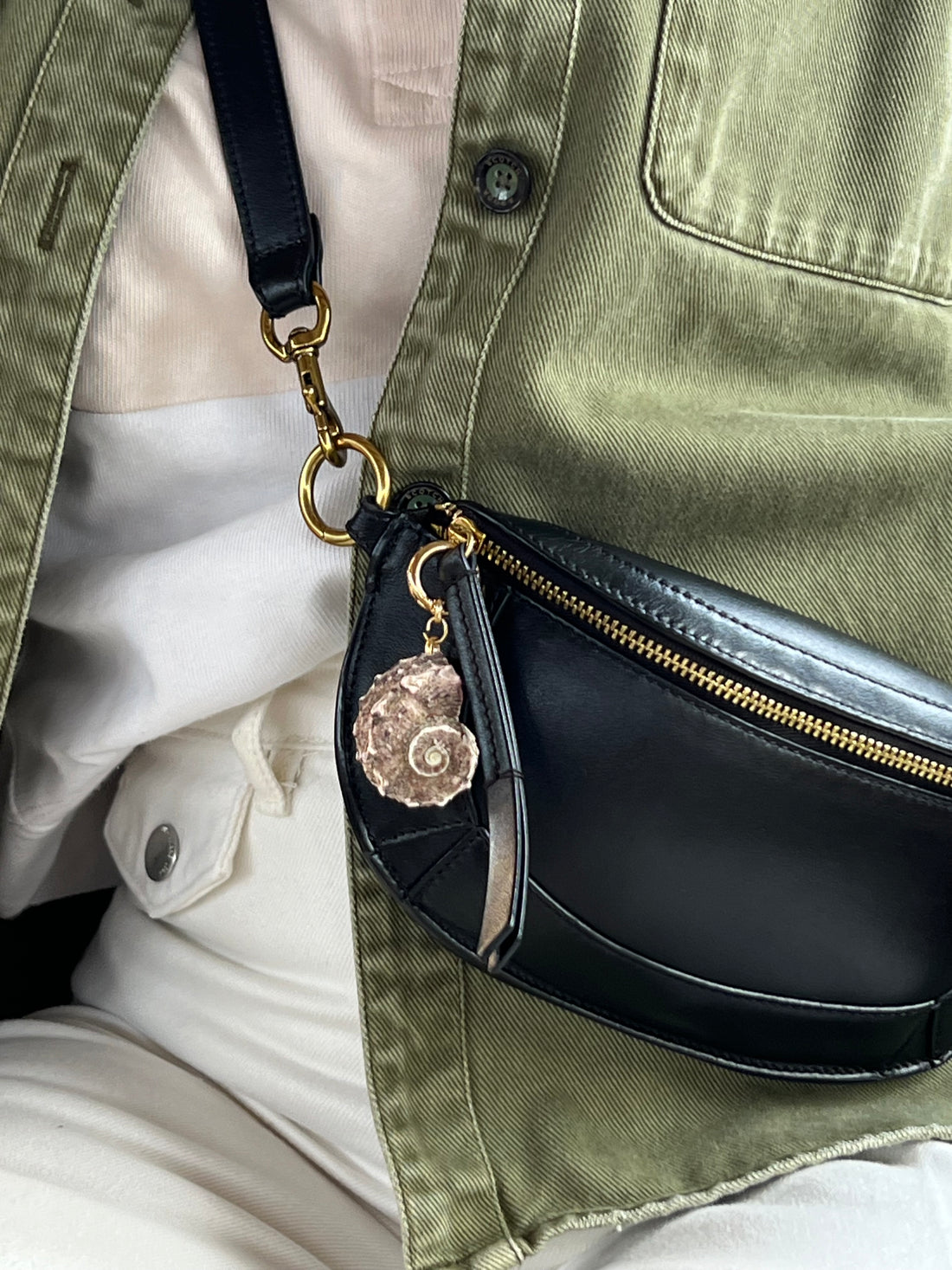 Handcrafted fob featuring a natural, textured spiral shell in earthy purple and grey tones, attached to a gold-toned spring ring styled on a black purse.