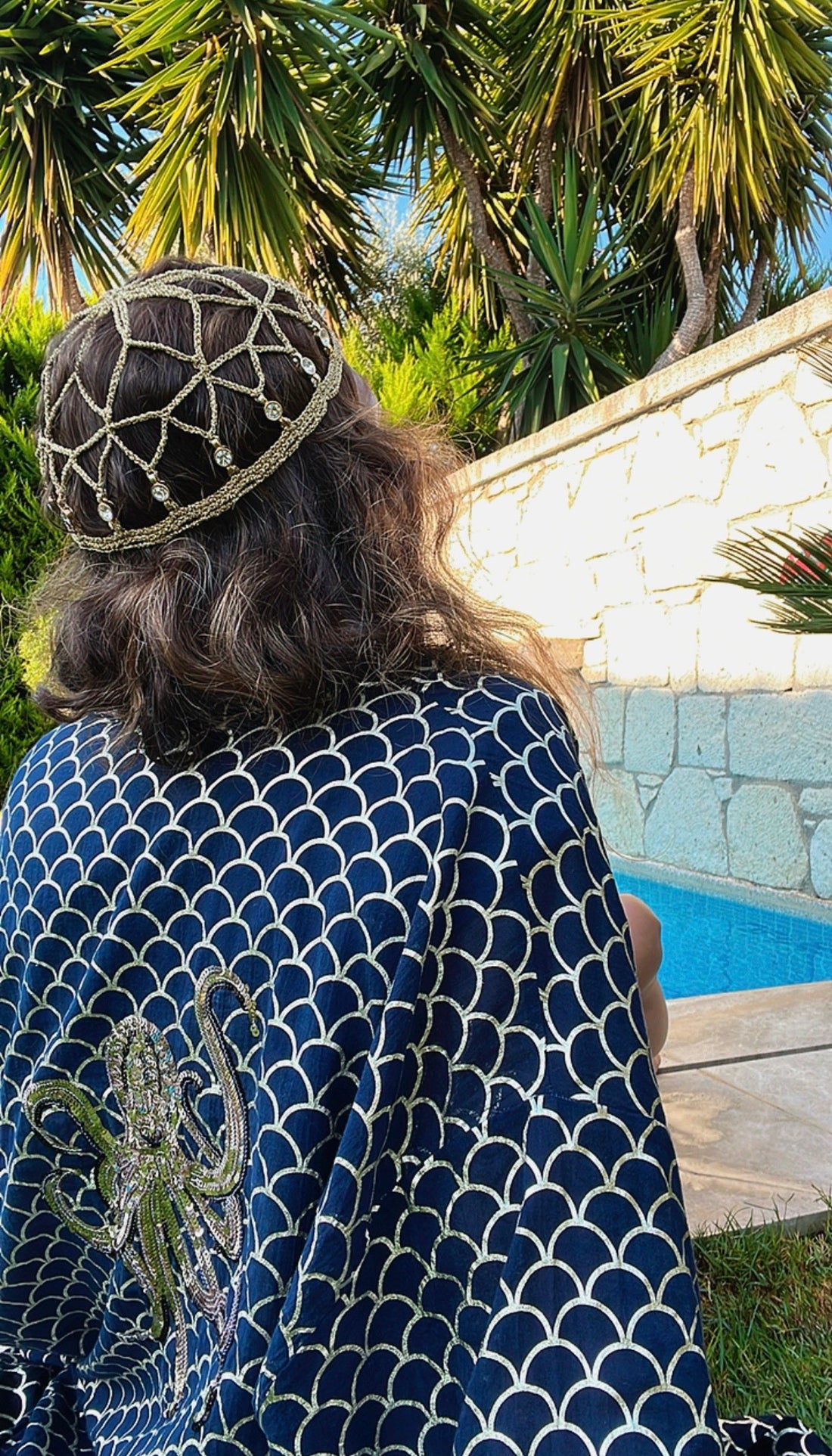 The gold headpiece styled with a scallop-patterned robe in a Mediterranean poolside setting.
