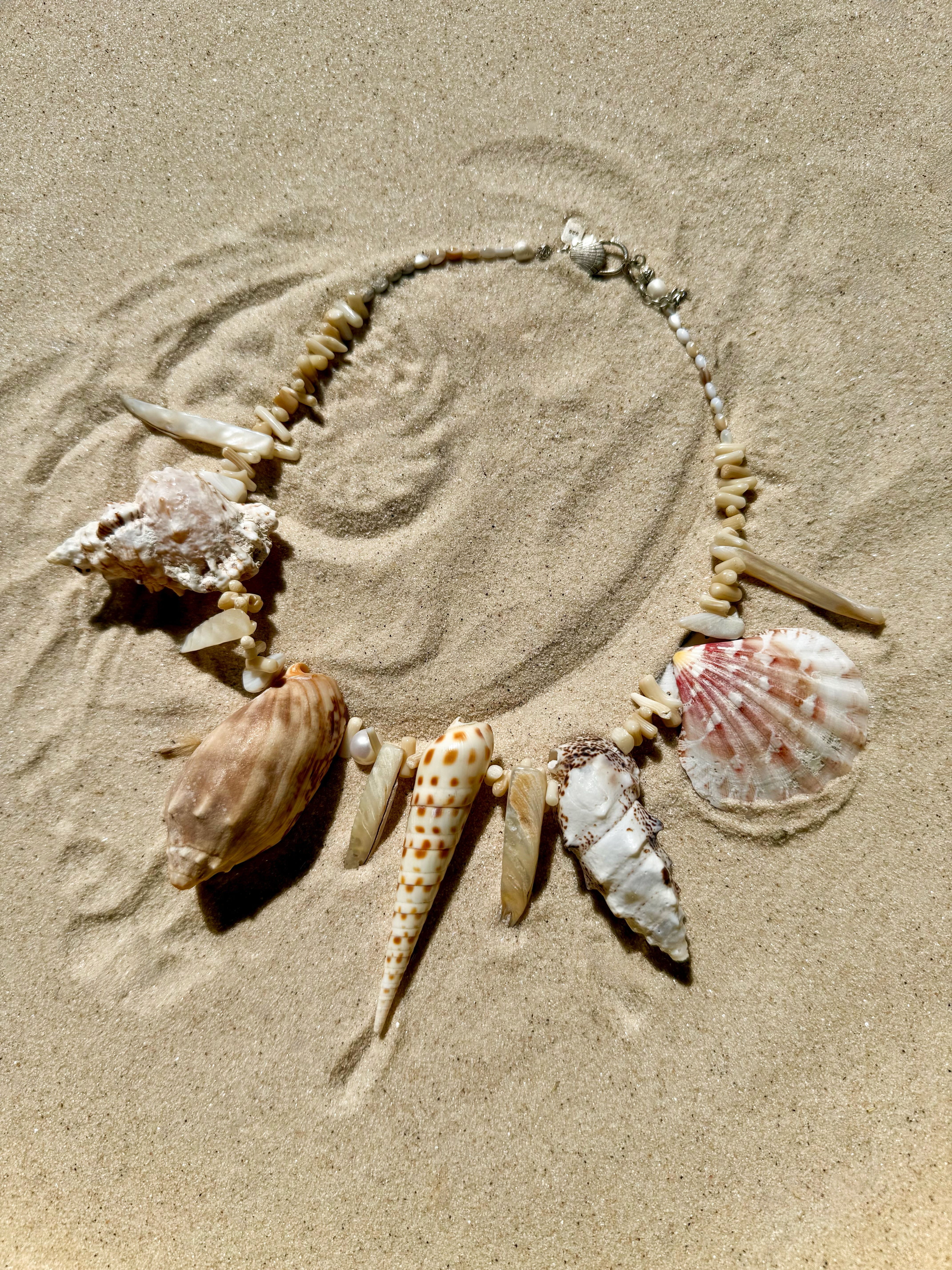 The Azurene Neckpiece artistically displayed on natural beach sand.
