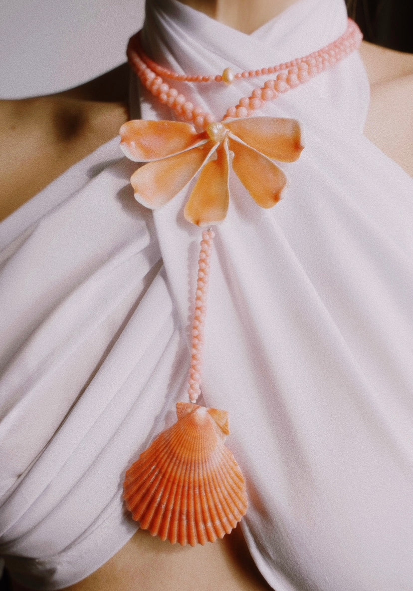 Handcrafted coral-toned beaded statement necklace featuring a sculptural shell flower and a large scallop shell pendant.