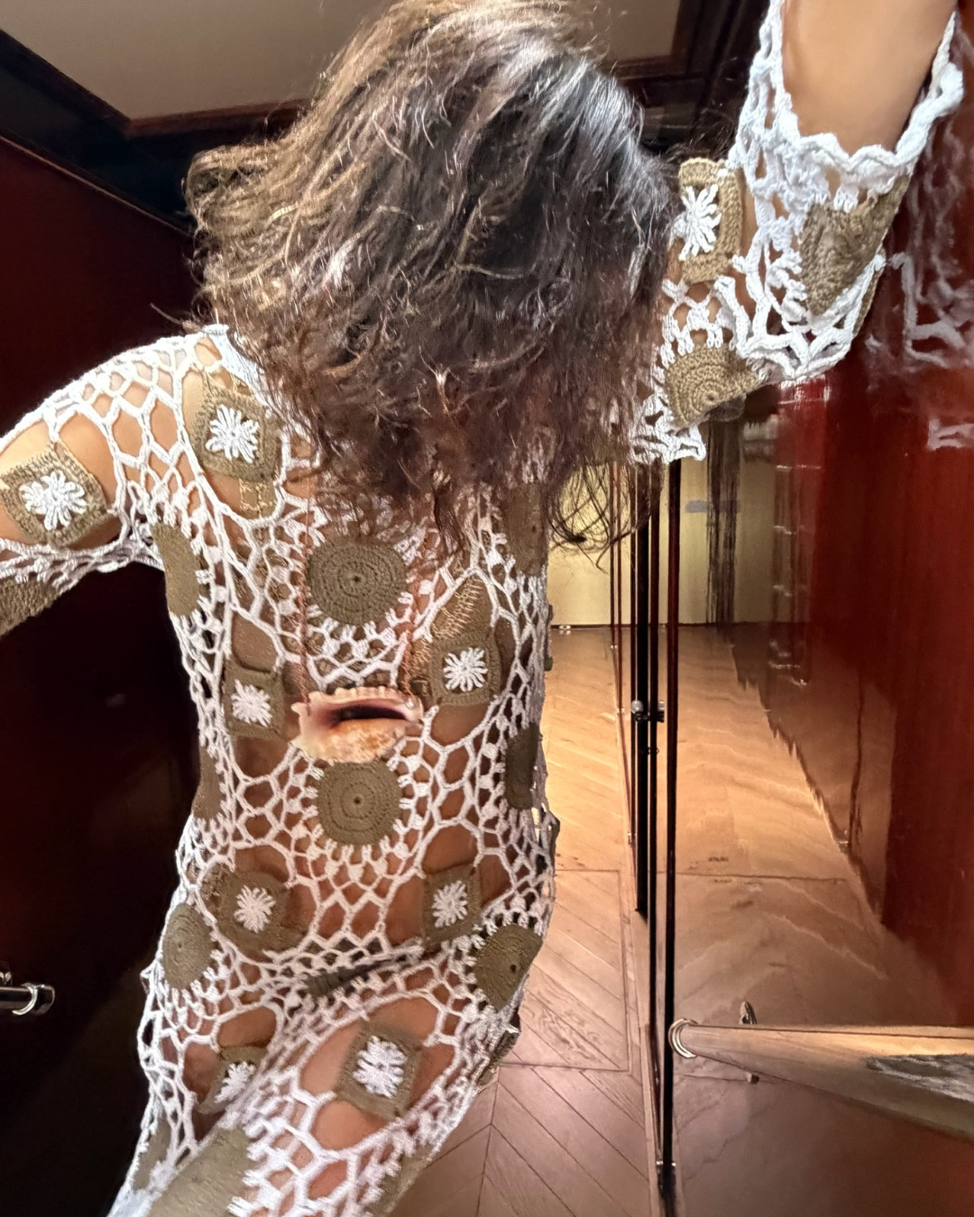 Woman wearing a crochet dress and the Cowrie Helmet Necklace posing in front of a mirror.