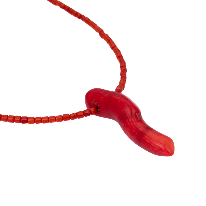 Close-up of the handcrafted red coral bead necklace and its sculptural, horn-shaped coral pendant against a white background.
