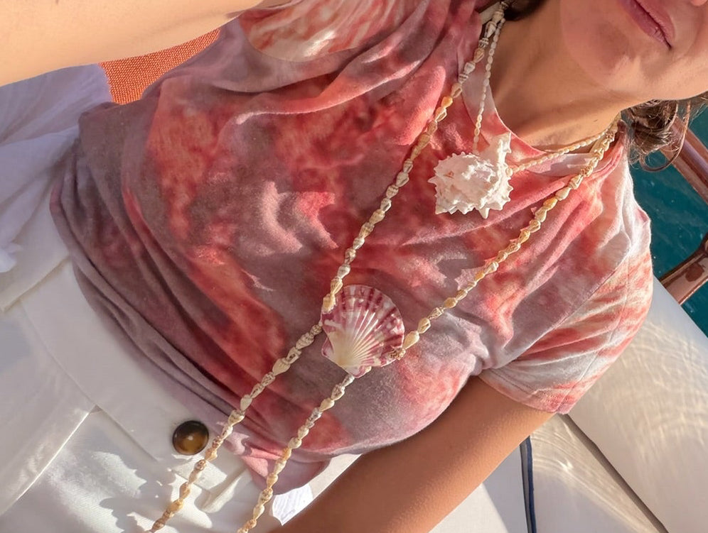 Handcrafted shell necklace featuring a central scallop shell and a strand of tiny shells, finished with white pearls and pink Madagascar rose quartz drops styled on a model.