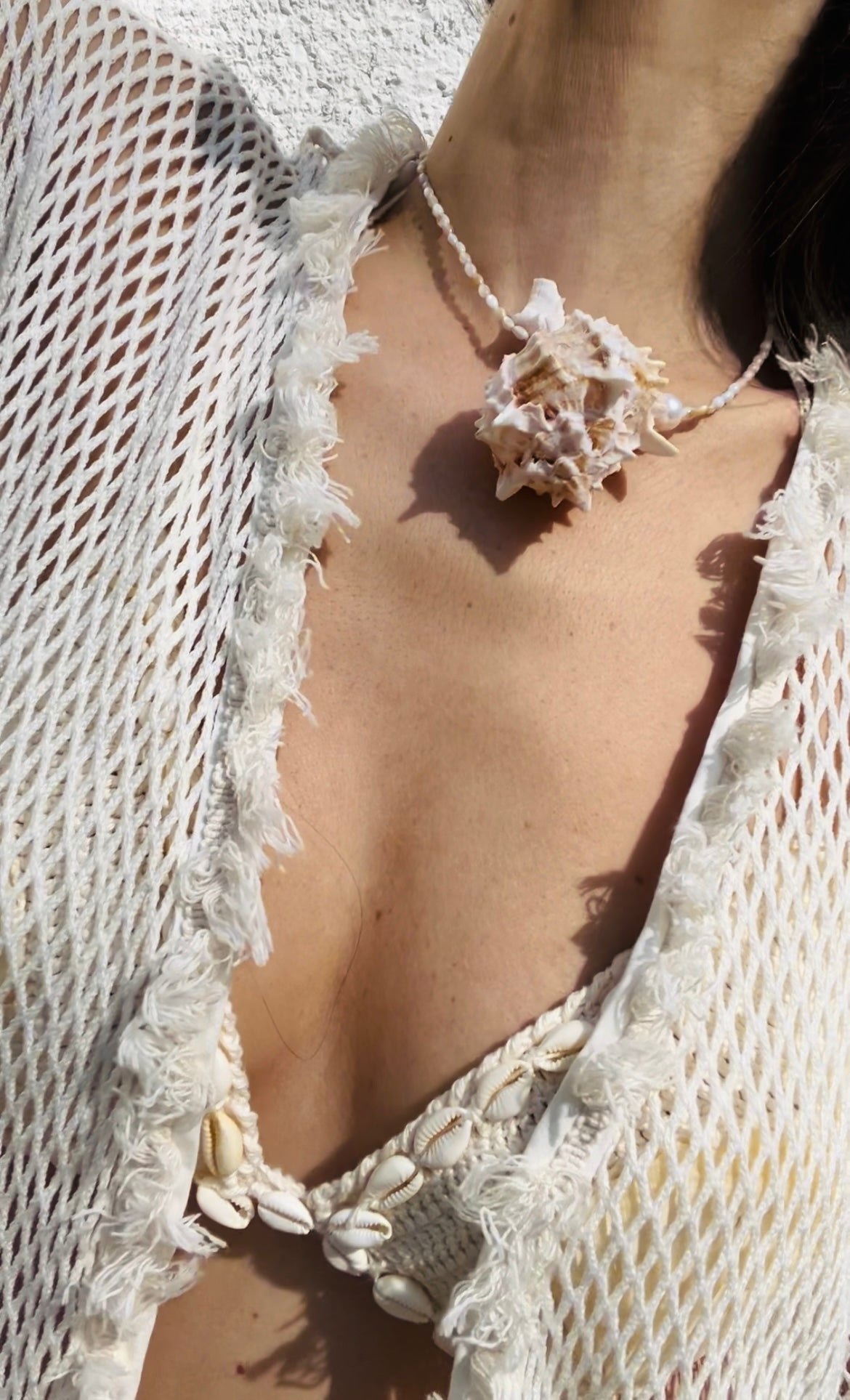 Lifestyle image of the statement necklace worn by a model, featuring a large murex shell pendant styled against coastal-inspired crocheted fashion.