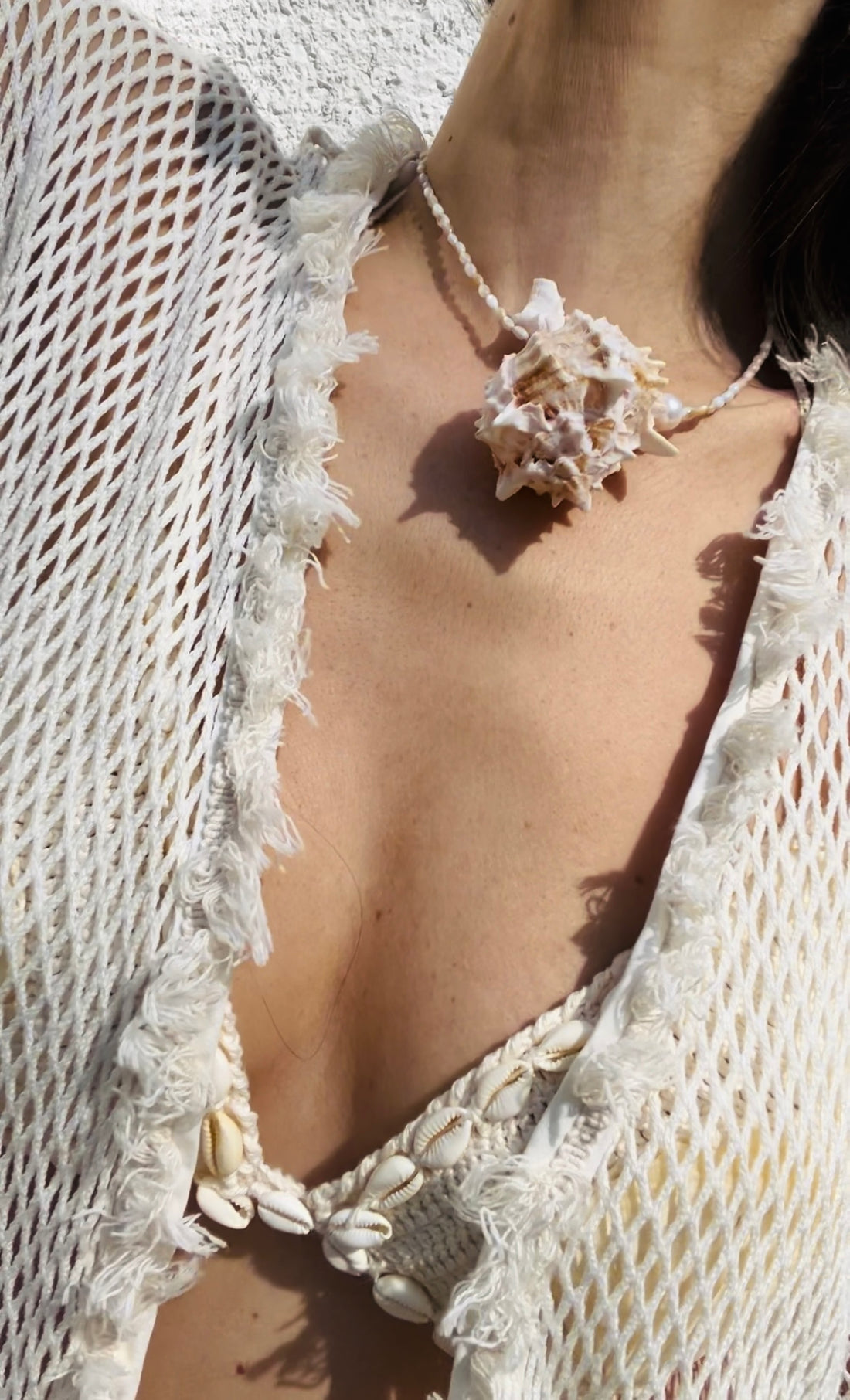 Lifestyle image of the statement necklace worn by a model, featuring a large murex shell pendant styled against coastal-inspired crocheted fashion.