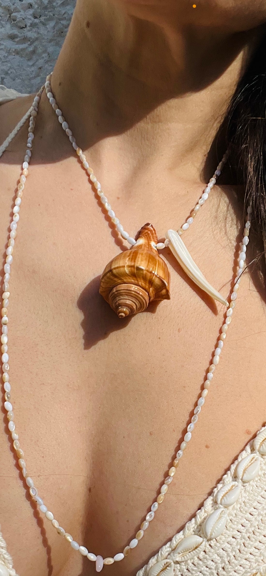 Lifestyle styling of the shell pendant necklace layered with fine beads for an elevated maritime look.