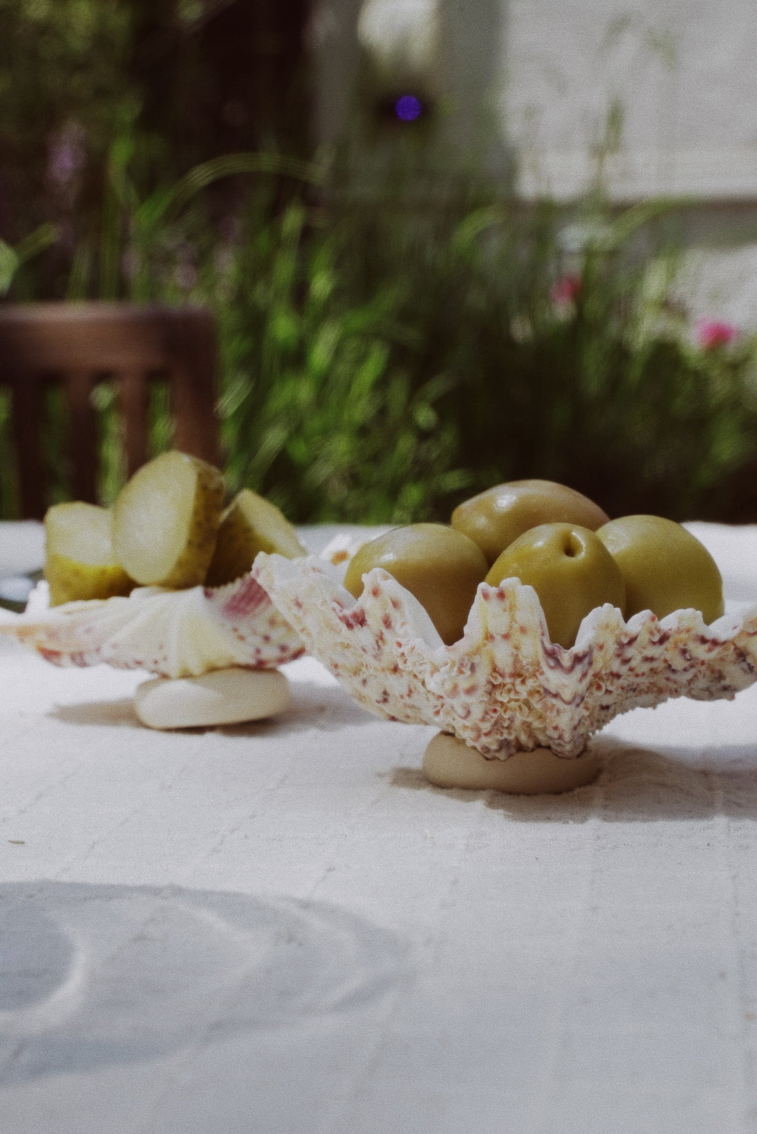 Two white clam shell-shaped serving bowls with a textured surface, displayed on a linen tablecloth. 