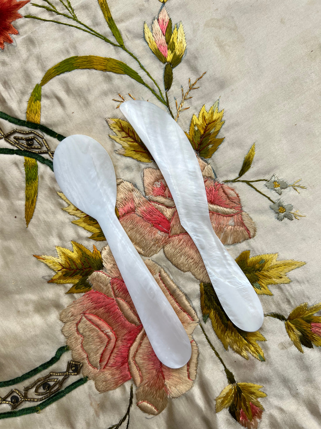 A set of flatware from mother of pearl , featuring a decorative floral pattern on the fabric background.