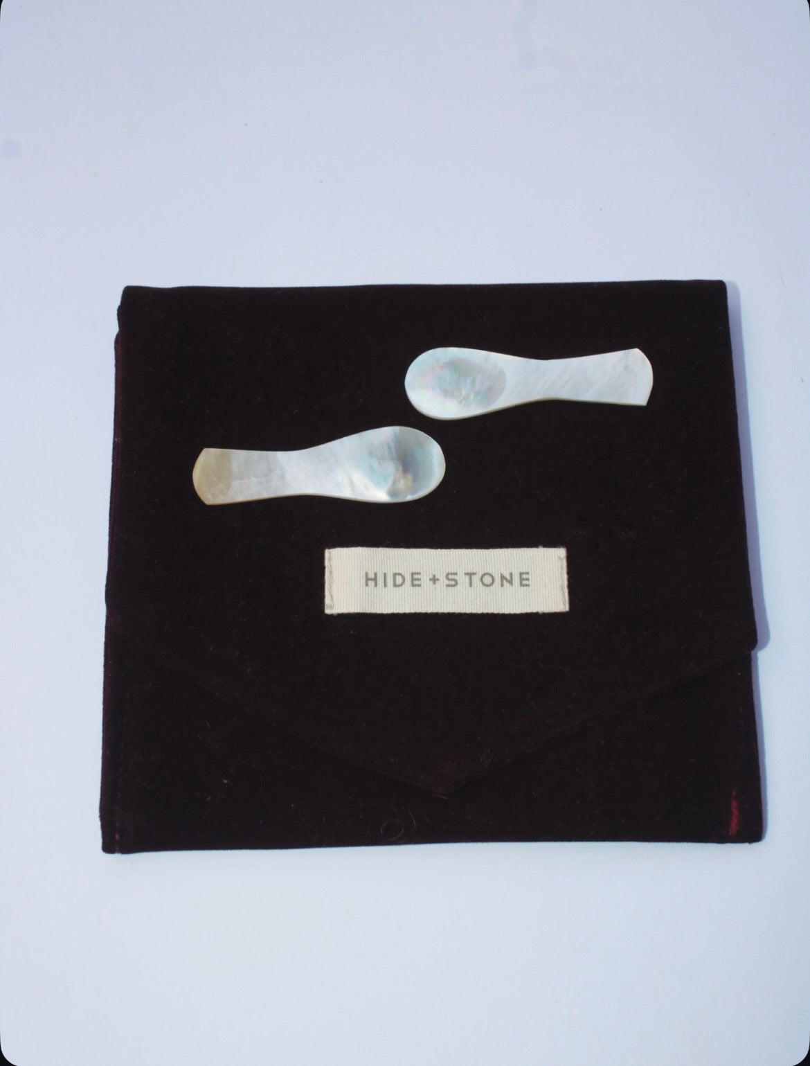 Black pouch with 2 spoons handcrafted from luminous pearl shell. 'HIDE + STONE' label on a white background