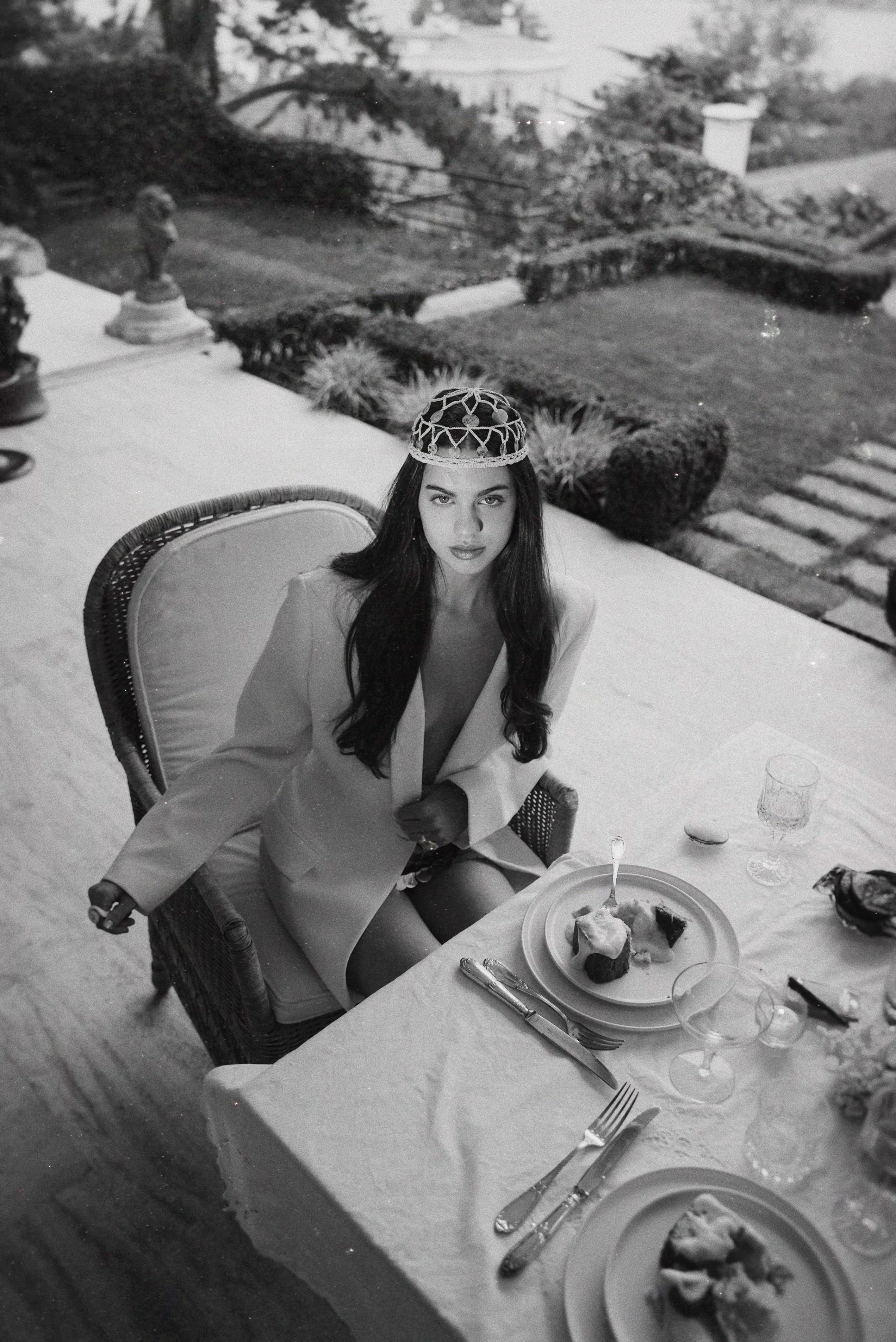 Atmospheric lifestyle shot of the crochet shell headpiece styled for a high-fashion outdoor dining setting.